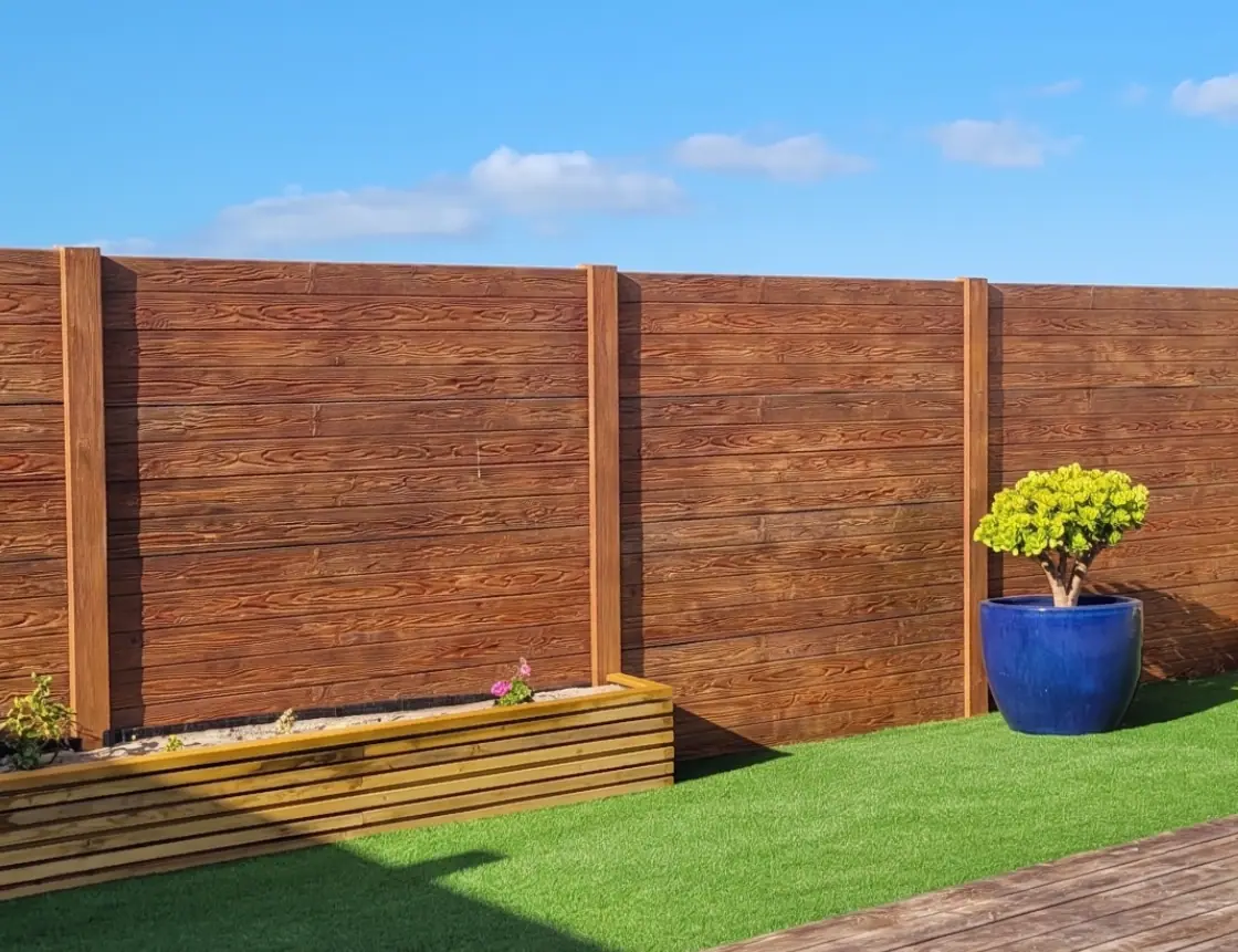 Precast concrete wall with wood texture in a dark shade, with flower beds and lawn in a garden