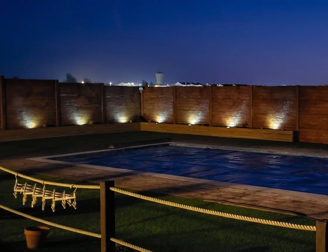 Precast concrete wall with grazing lighting beside a pool, at dusk